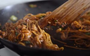 Stir-fried noodles, glistening with sauce, are tossed in a hot pan