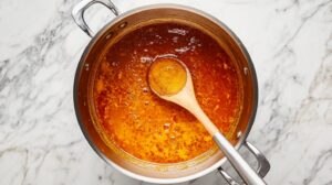 A pot of simmering orange curry with a wooden spoon on a marble countertop